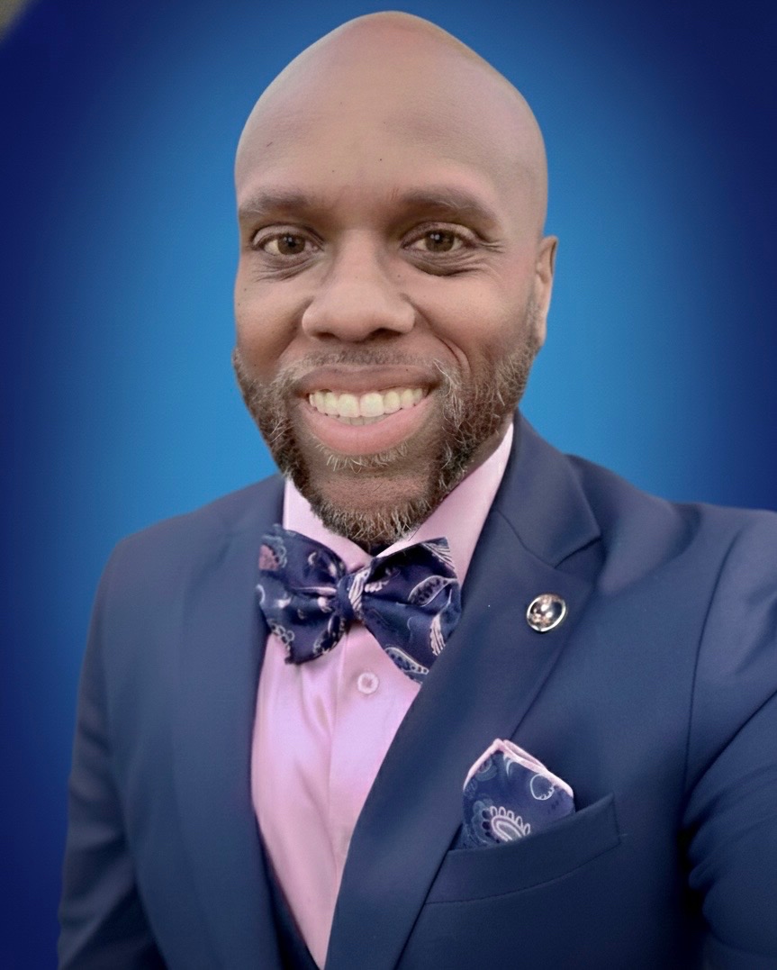 Miles Randall in a navy suit and bow tie, smiling confidently
